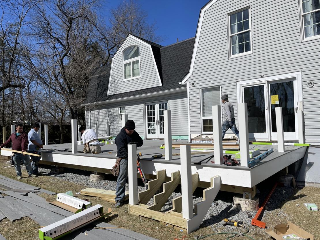 Crew setting posts and laying composite deck boards on a new deck frame