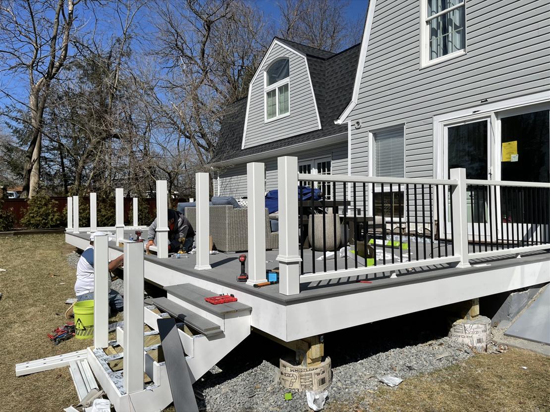 Installing white railing posts and black aluminum balusters on the finished deck surface